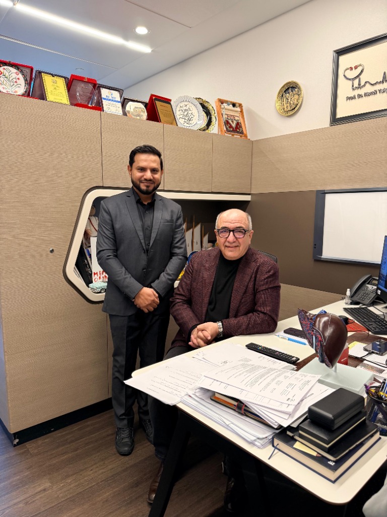 إعجاز أحمد واقفًا بجانب زميل يجلس إلى مكتبه